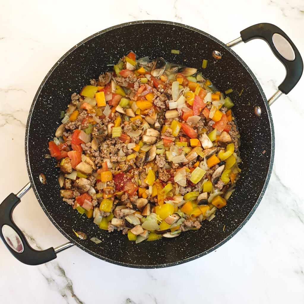 Mushrooms and tomatoes added to the meat and vegetables in a frying pan.