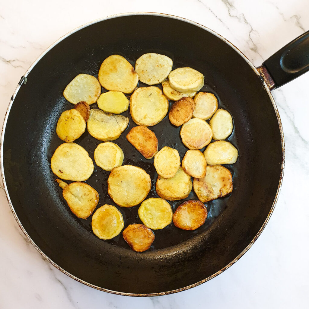 Sliced potatoes browning in a frying pan.