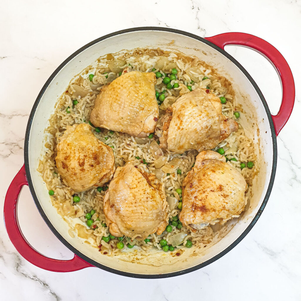 5 pieces of chicken in a pan on a bed of rice and peas.