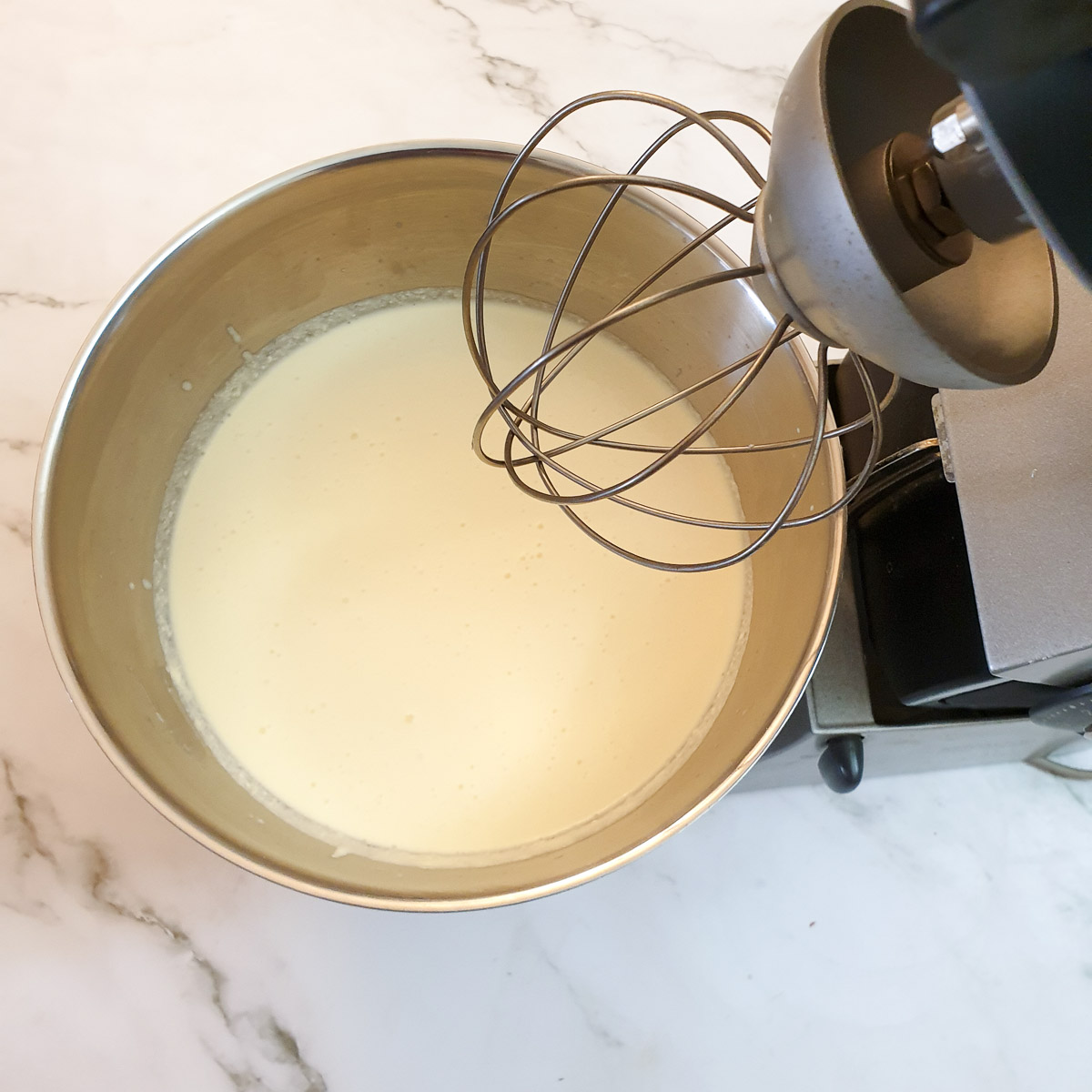 Double cream in a stand mixer fitted with a balloon whisk.