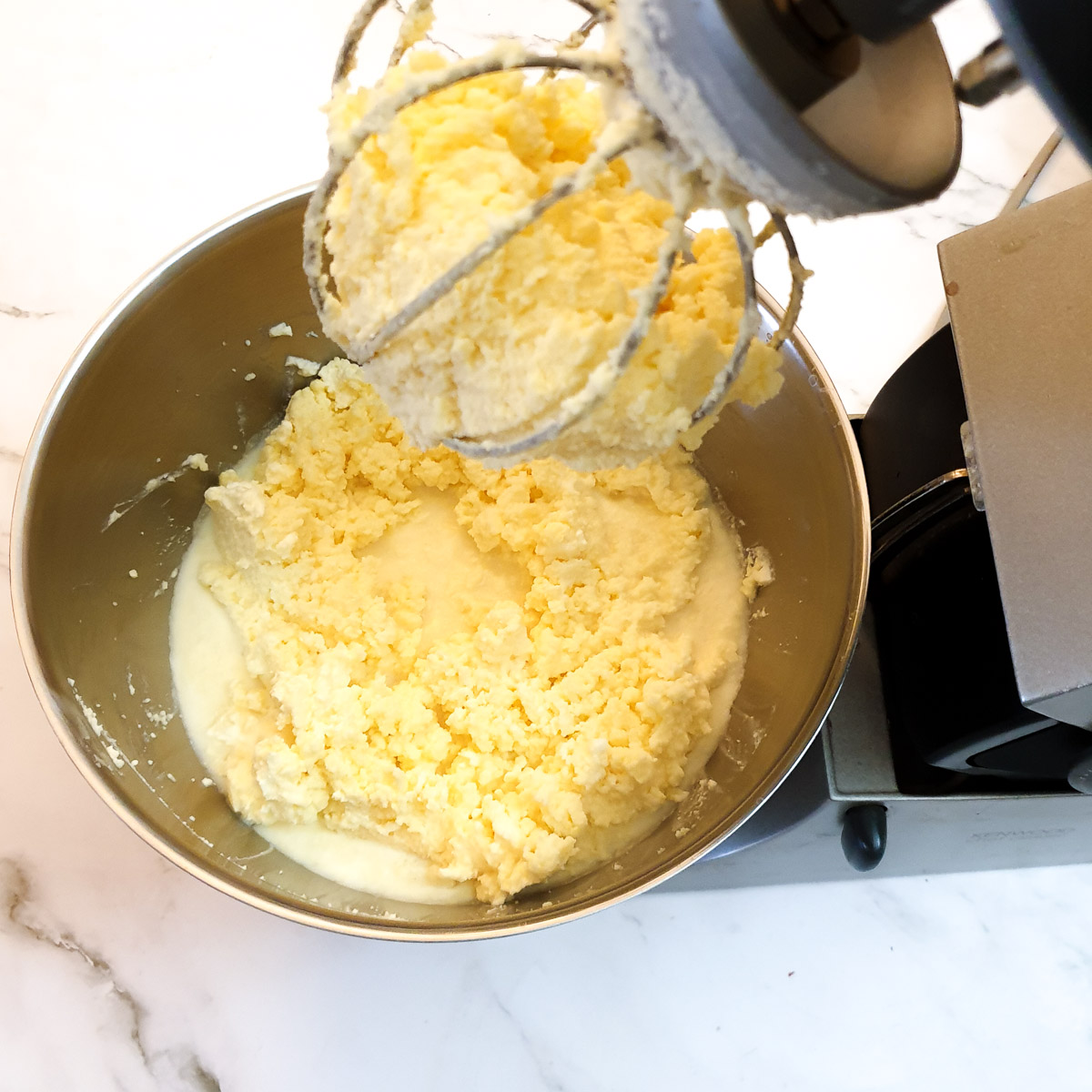 Homemade butter clinging to the whisk, with buttermilk remaining in the bowl of a stand mixer.