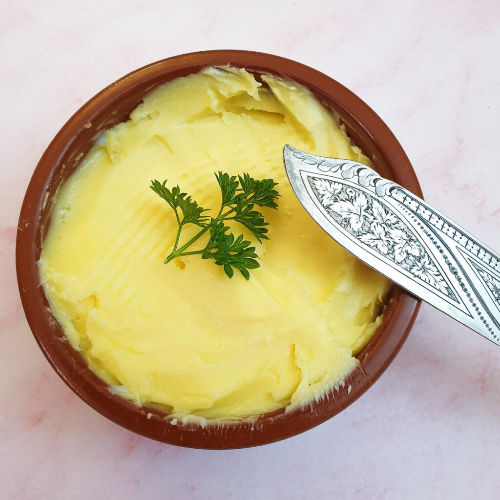 Close up of a dish of homemade butter, garnished with parsley.