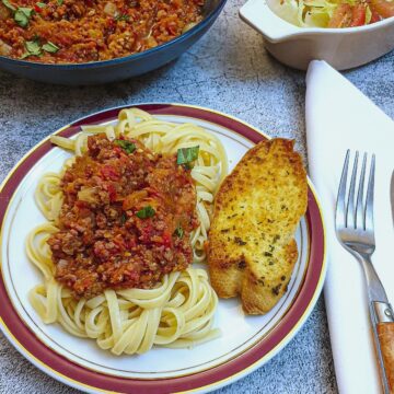 A plate of spaghetti with bolognese sauce and garlic bread.