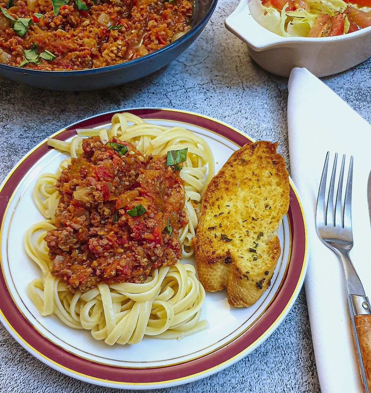 A plate of spaghetti with bolognese sauce and garlic bread.