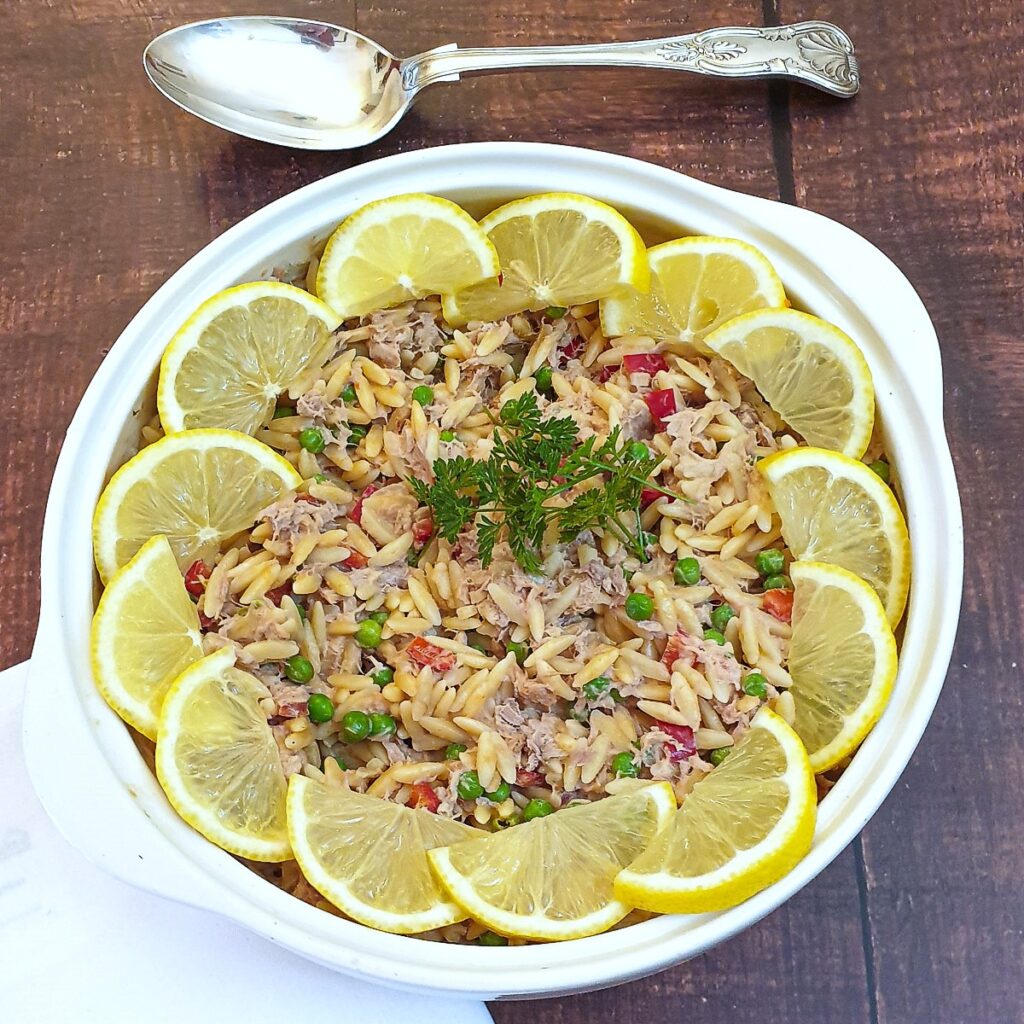 A bowl of tuna noodle pasta garnished with lemon slices.