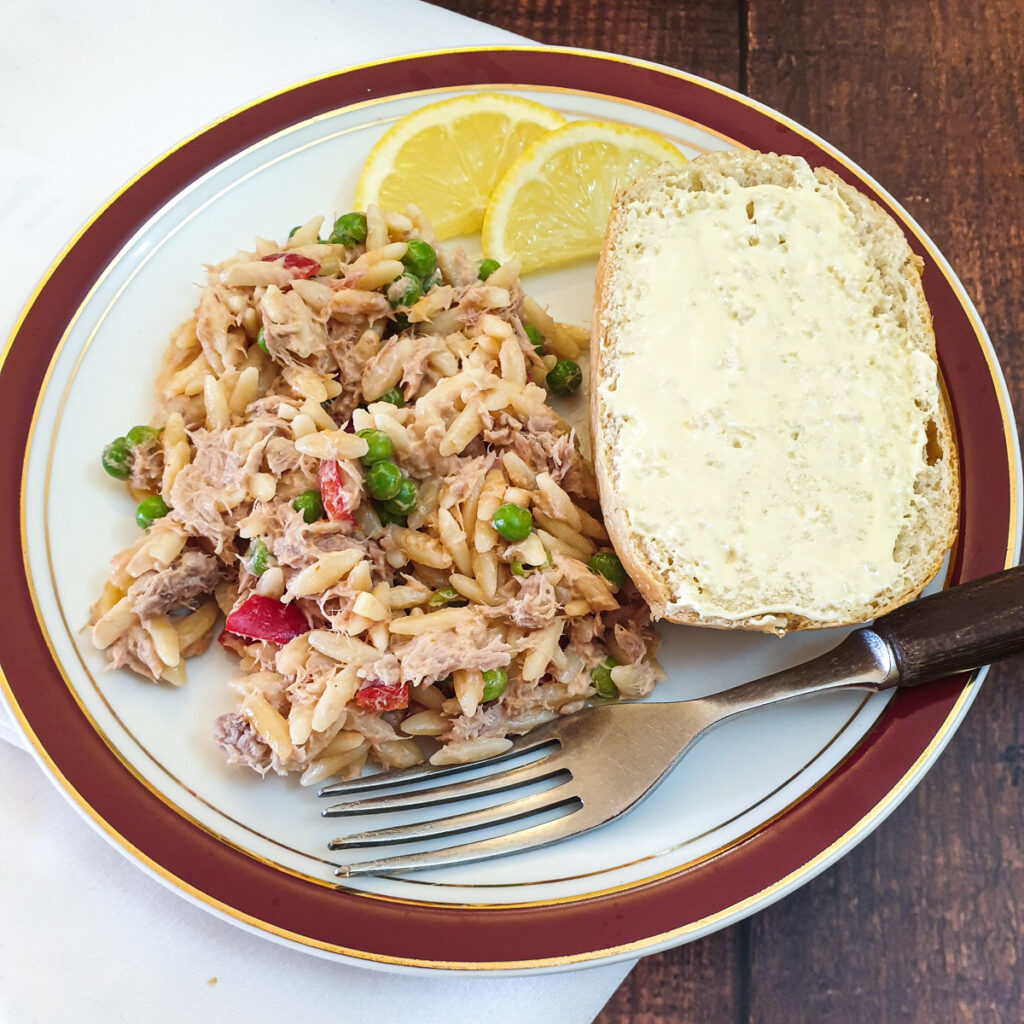 A helping of tuna noodle salad on a plate with a slice of crusty bread roll.