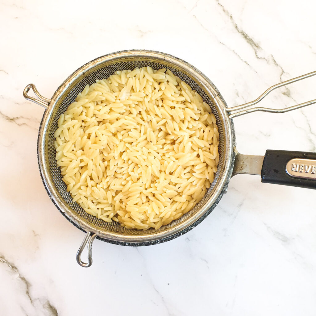 Orzo pasta draining in a sieve.