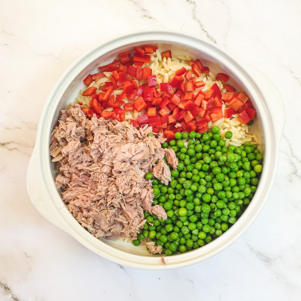 Orzo pasta in a bowl with peas, tuna and chopped red peppers.