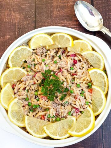 A bowl of tuna noodle pasta garnished with lemon slices.