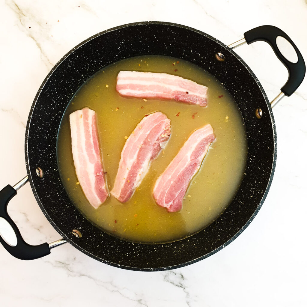 Pork belly rashers in a pan of stock.