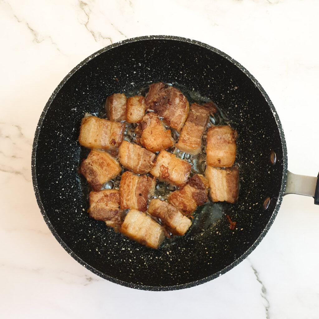 Cubes of pork belly browning in a frying pan.