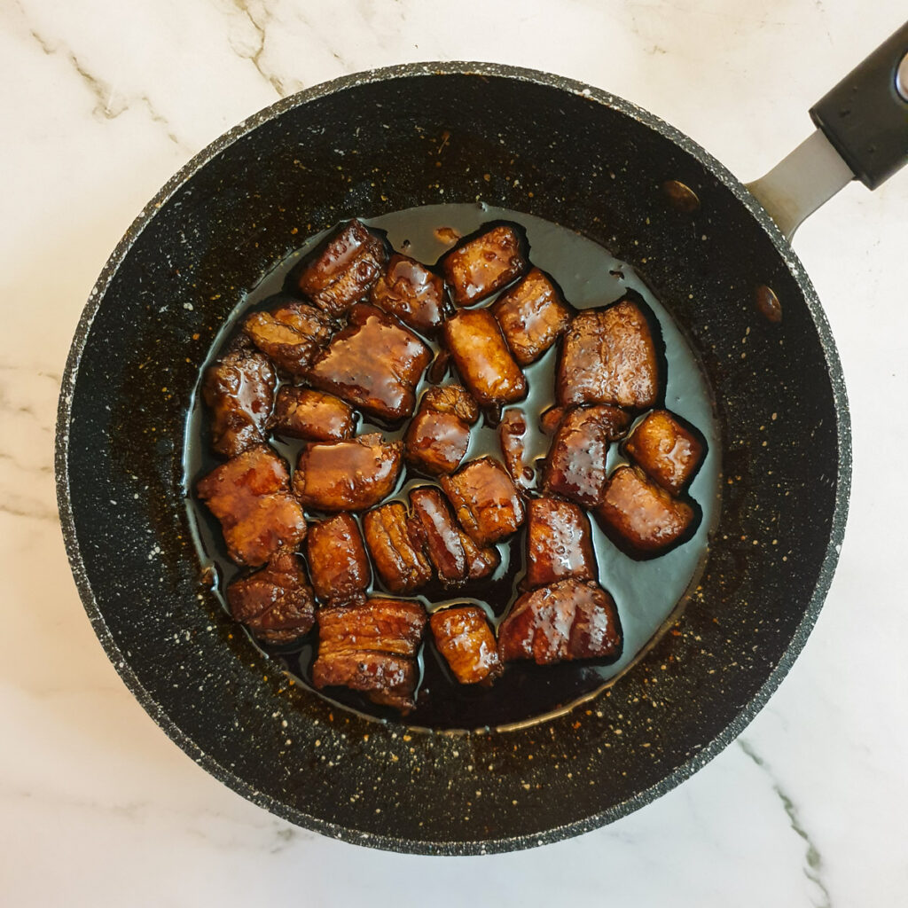 Pork belly cubes covered with glaze in a frying pan.