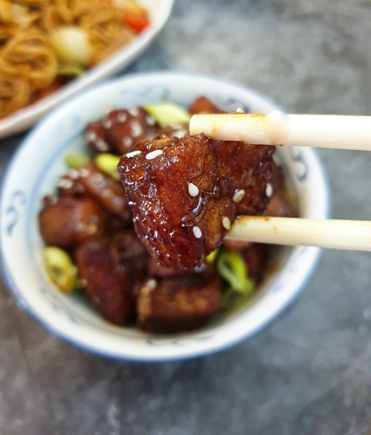 Close up of a piece of sticky pork belly held in chopsticks.