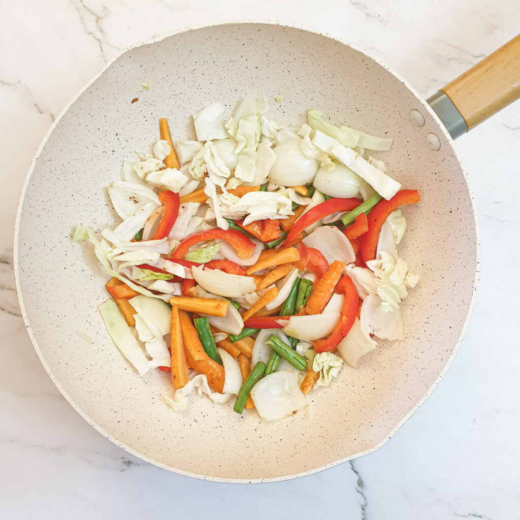 Sliced cabbage, red peppers, onions, carrots and green beans in a frying pan.