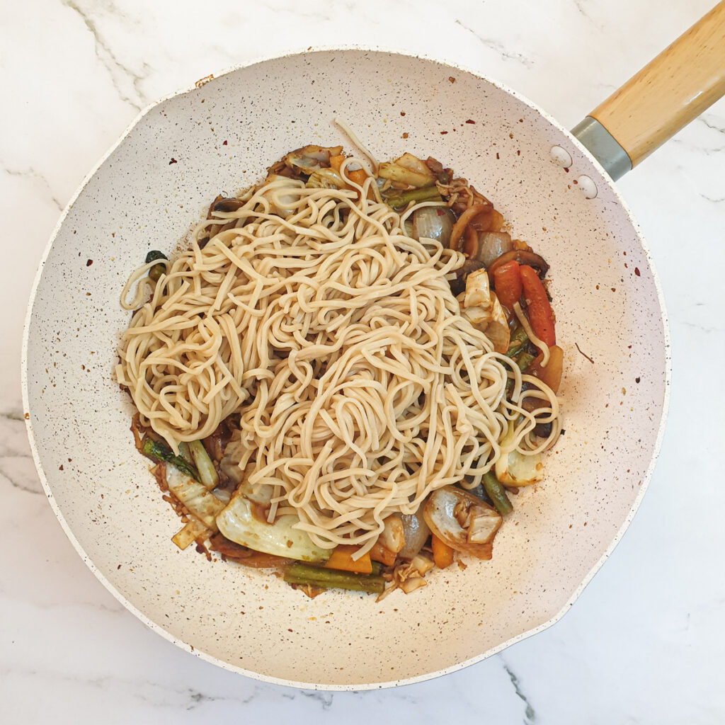 Cooked noodles being added to the vegetable lo mein.