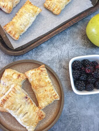 Three apple and blalckberrry turnovers on a plate.