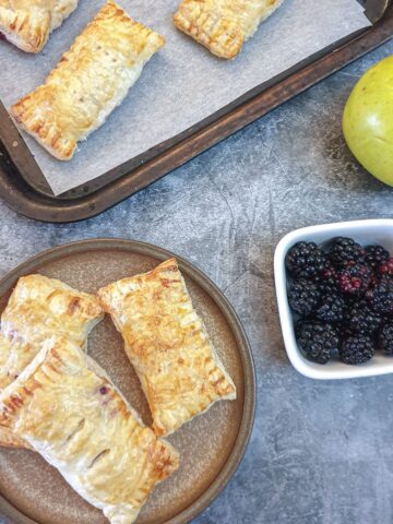 Three apple and blalckberrry turnovers on a plate.