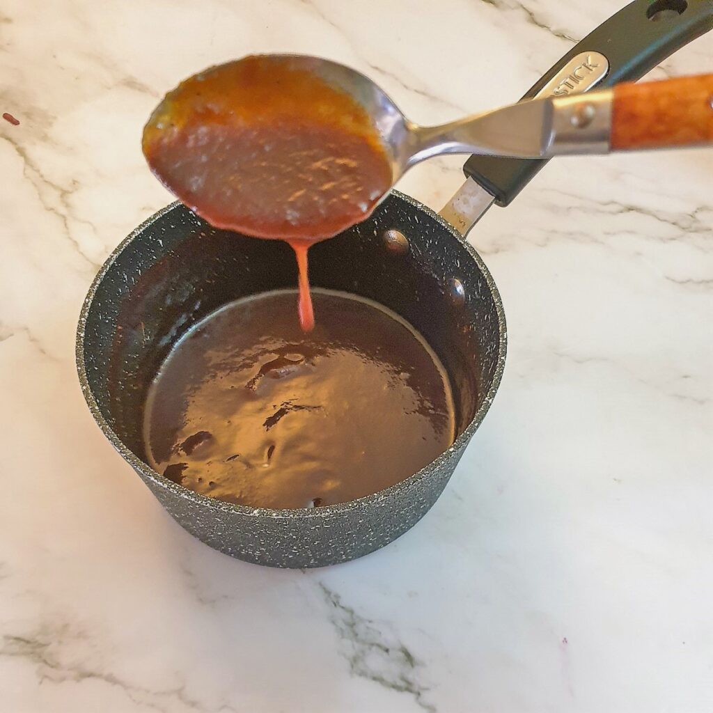 A spoonful of barbeque sauce over a saucepan pan showing the consistency.