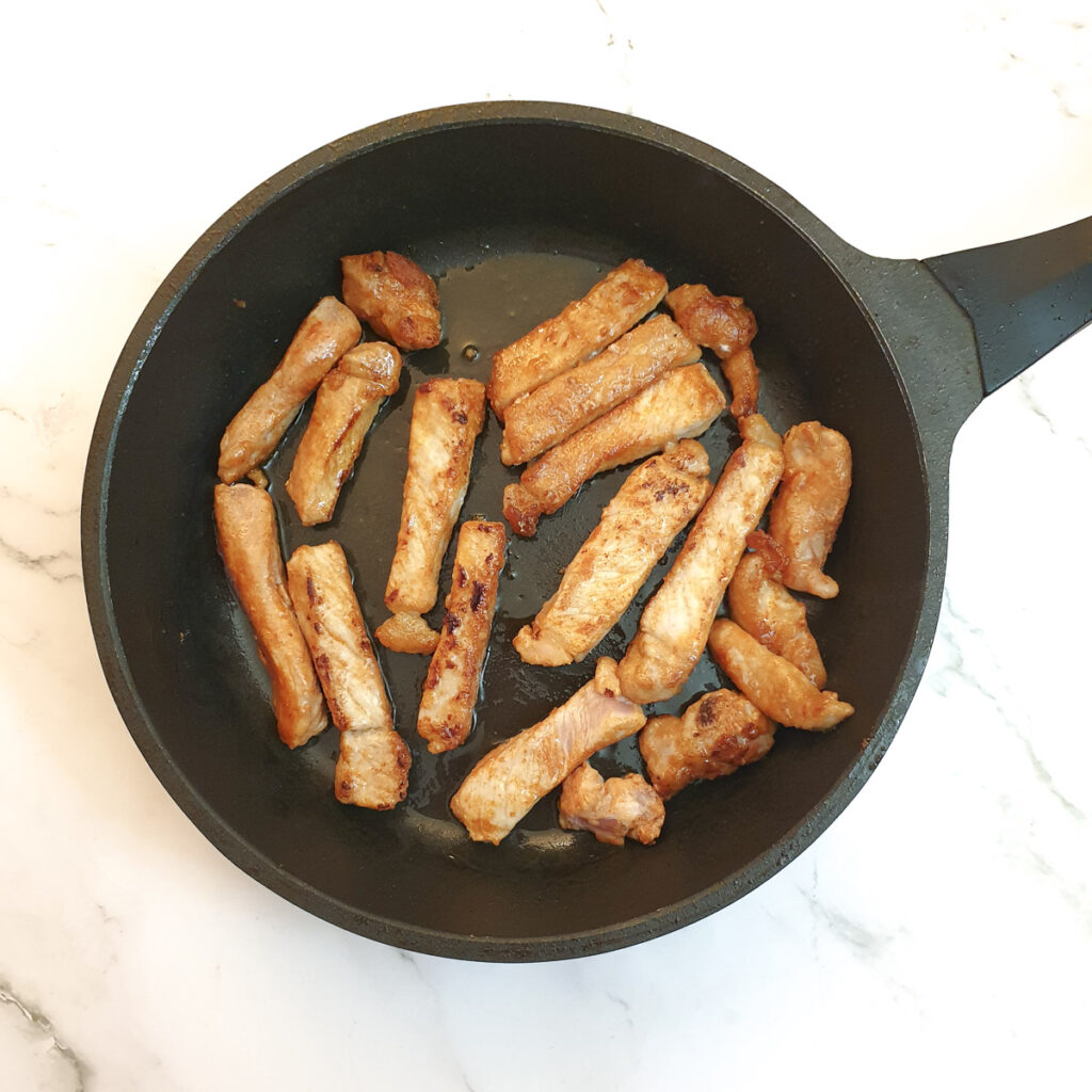 Fingers of pork loin being browned in a frying pan.