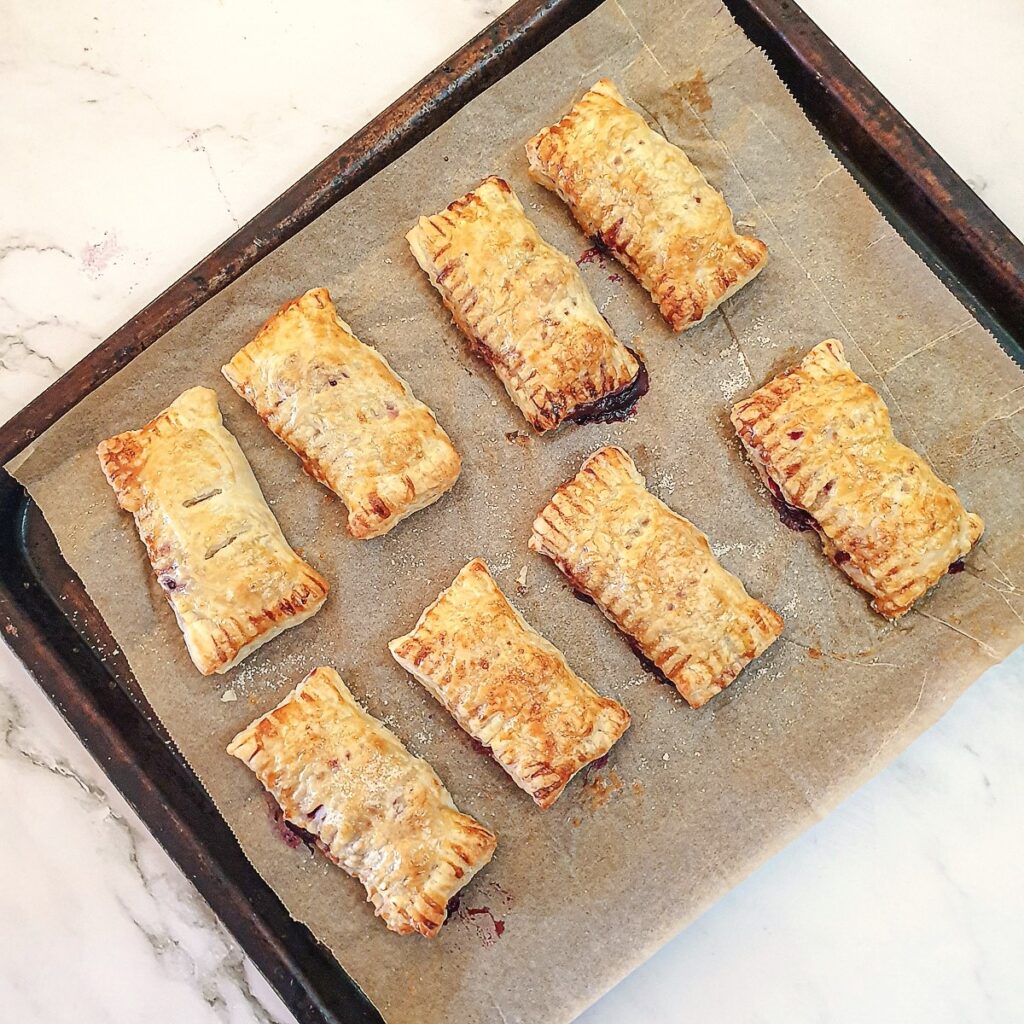 A baking tray with 8 baked apple and blackberry turnovers.