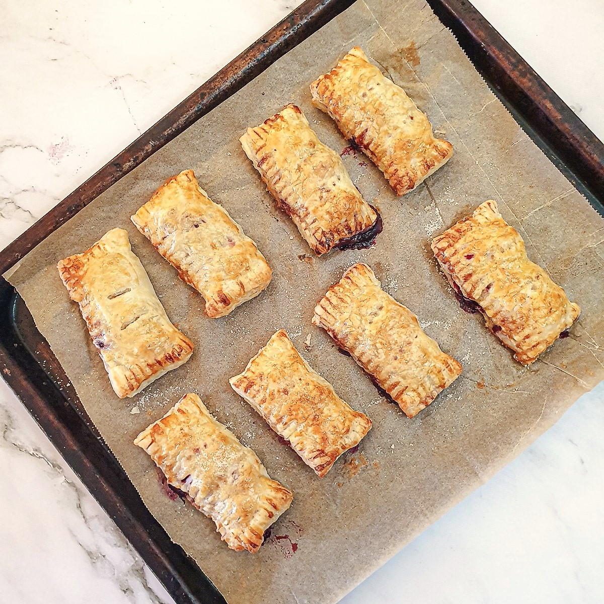 A baking tray with 8 baked apple and blackberry turnovers.