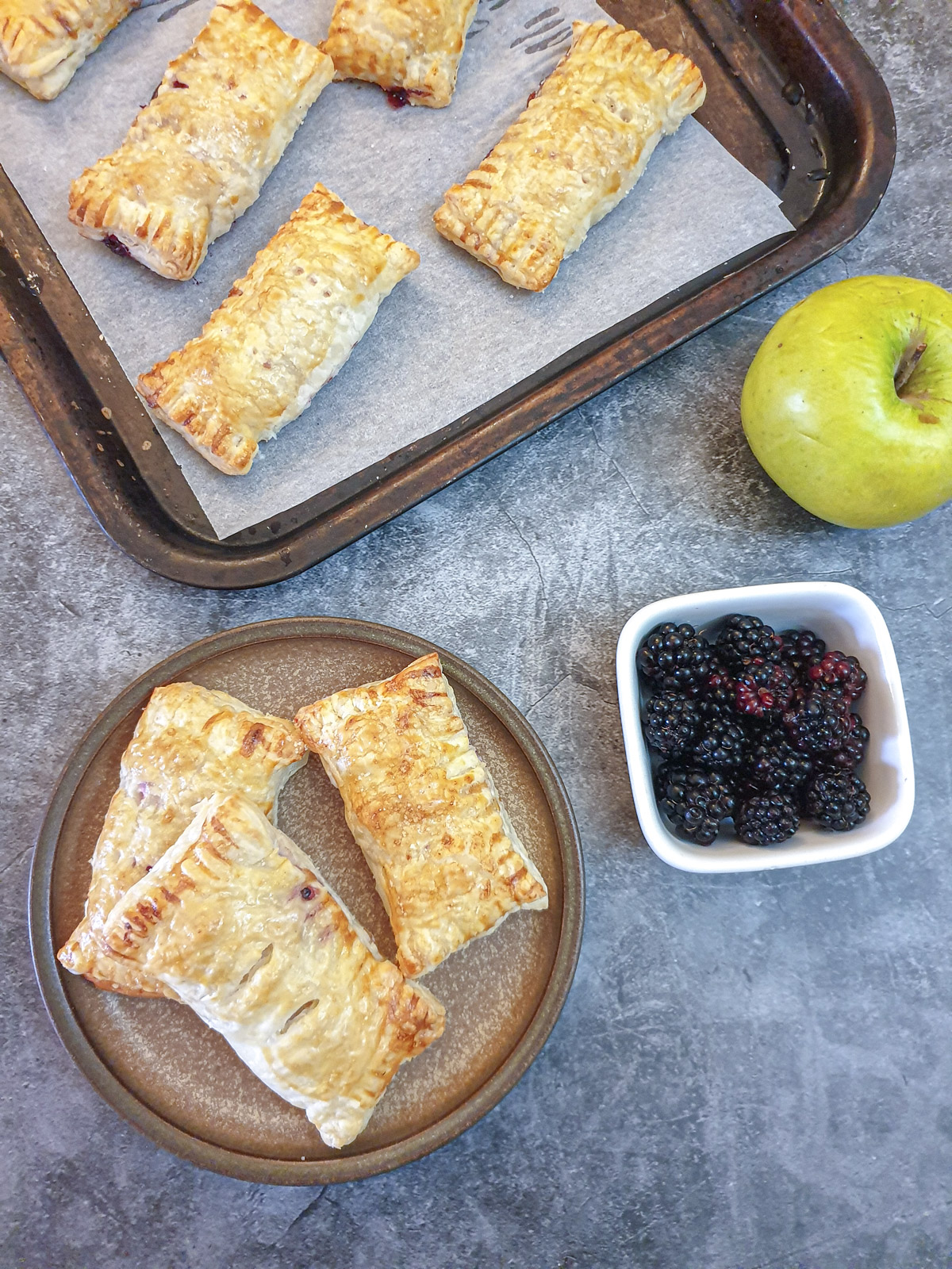 Three apple and blackberrry turnovers on a plate.