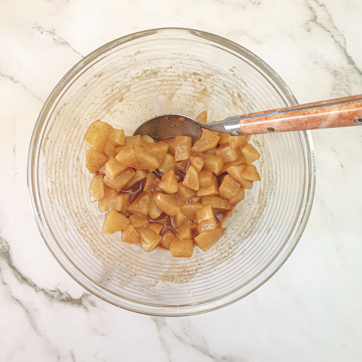 Cooked apples in a mixing bowl mixed with brown sugar and cinnamon.