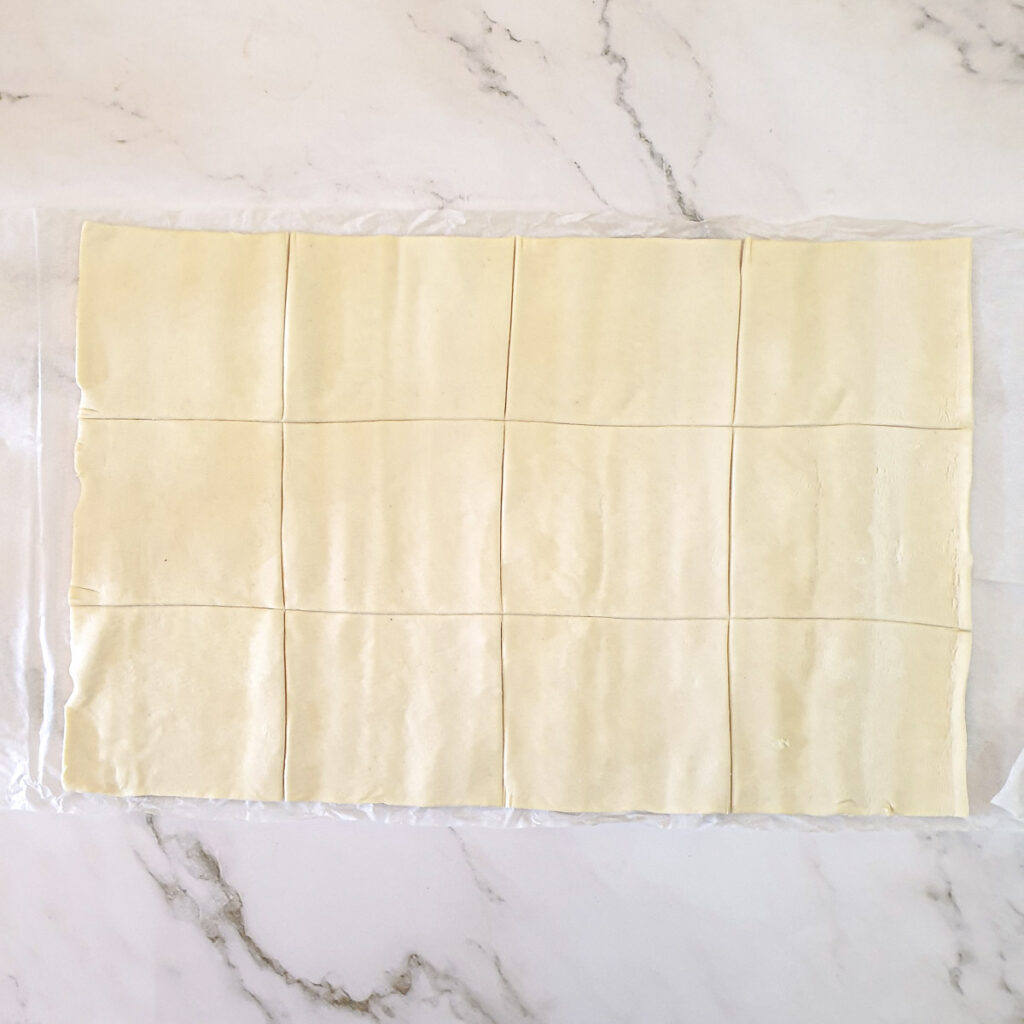 A sheet of puff pastry cut into 12 squares.