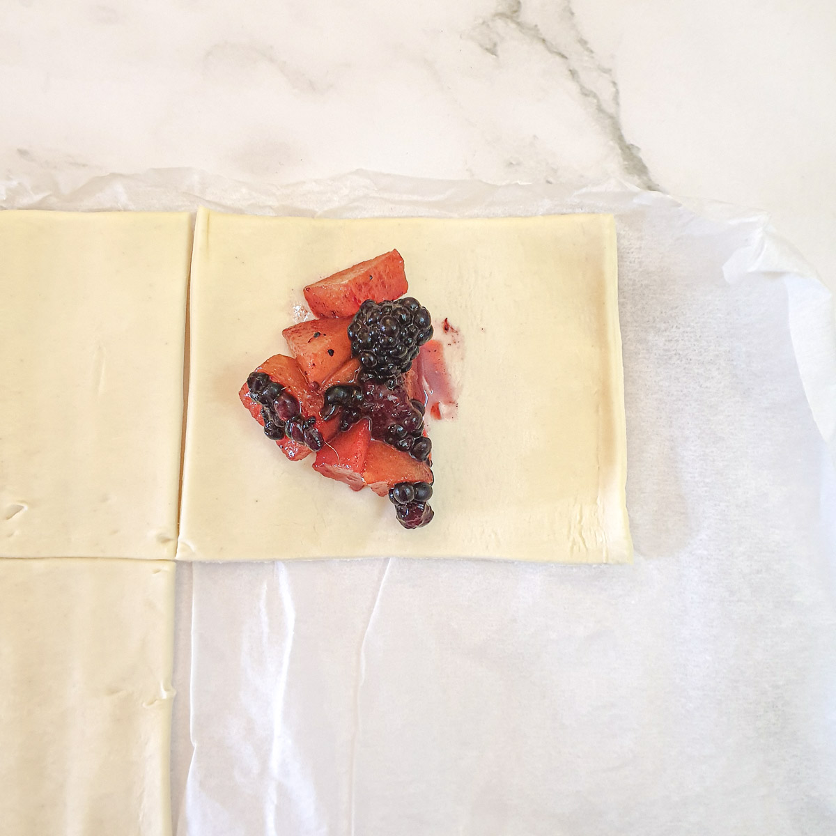 A tablespoon of blackberry and apple filling on a square of puff pastry.