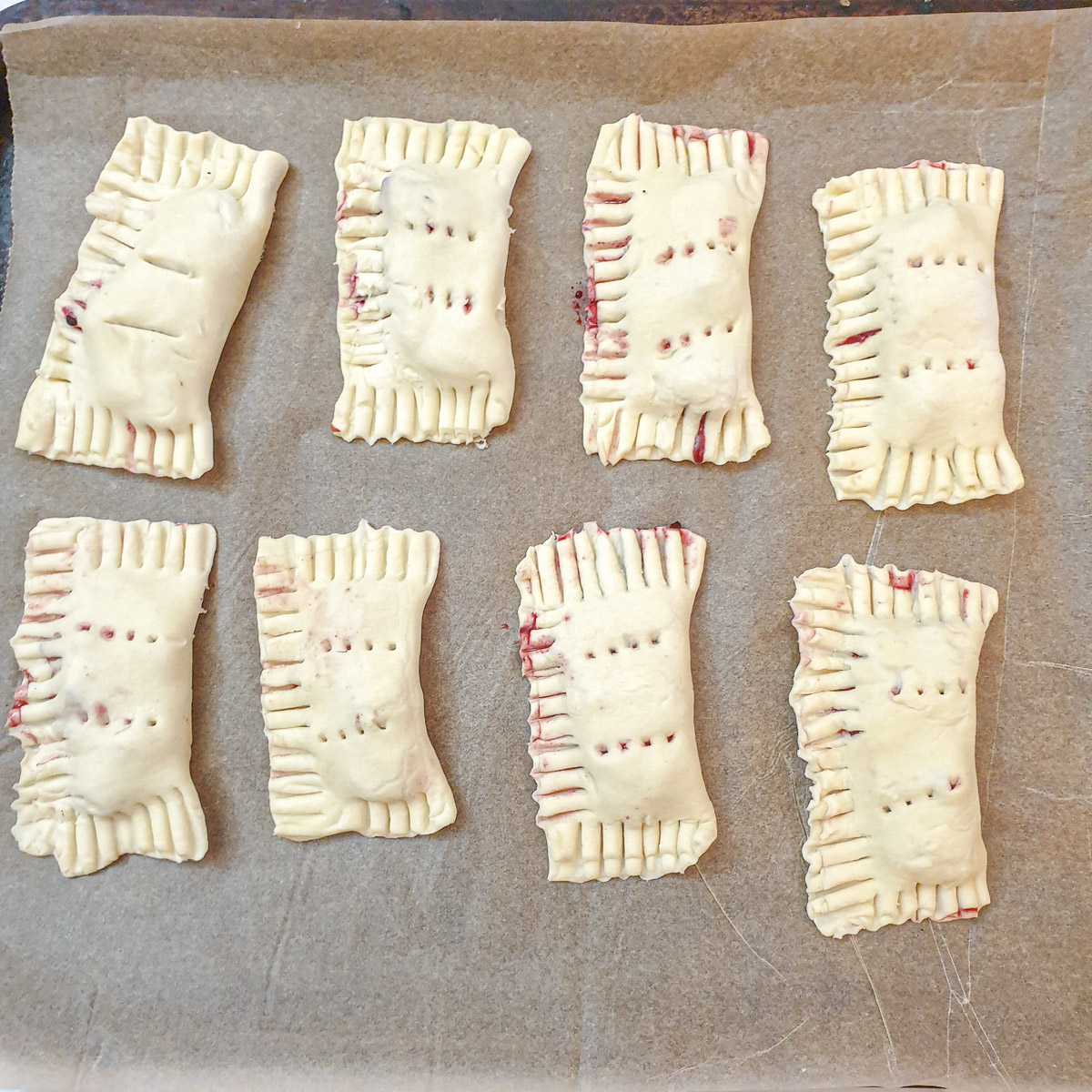 8 unbaked apple and blackberry turnovers on a baking tray.