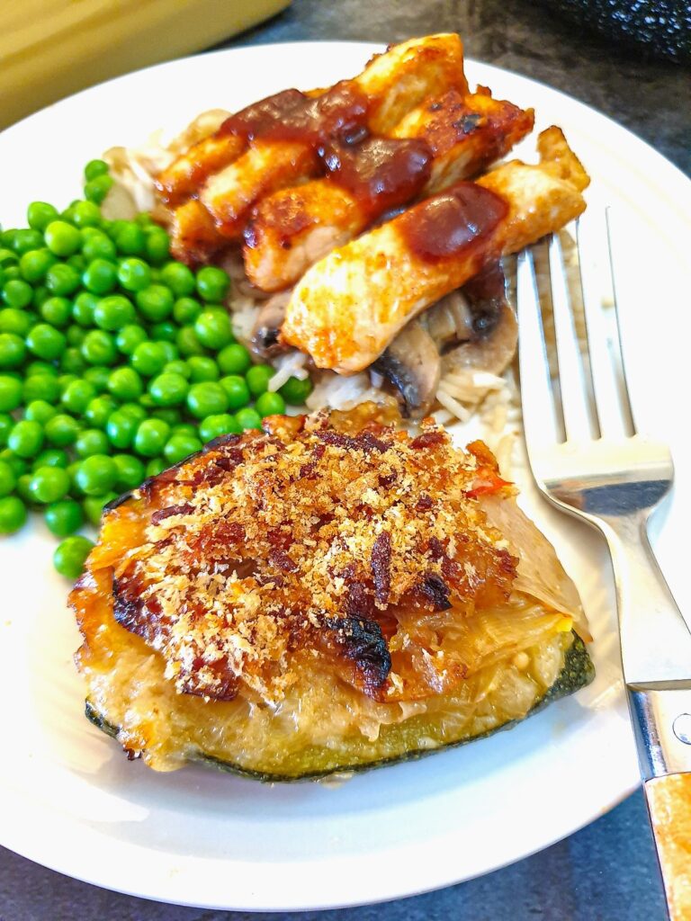 A cabbage-stuffed courgette on a plate with pork fingers, peas and mushroom rice.