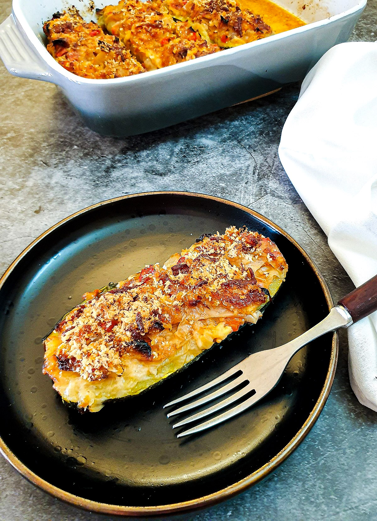 A cabbage-stuffed courgette with a cheesy topping on a brown plate with a fork.