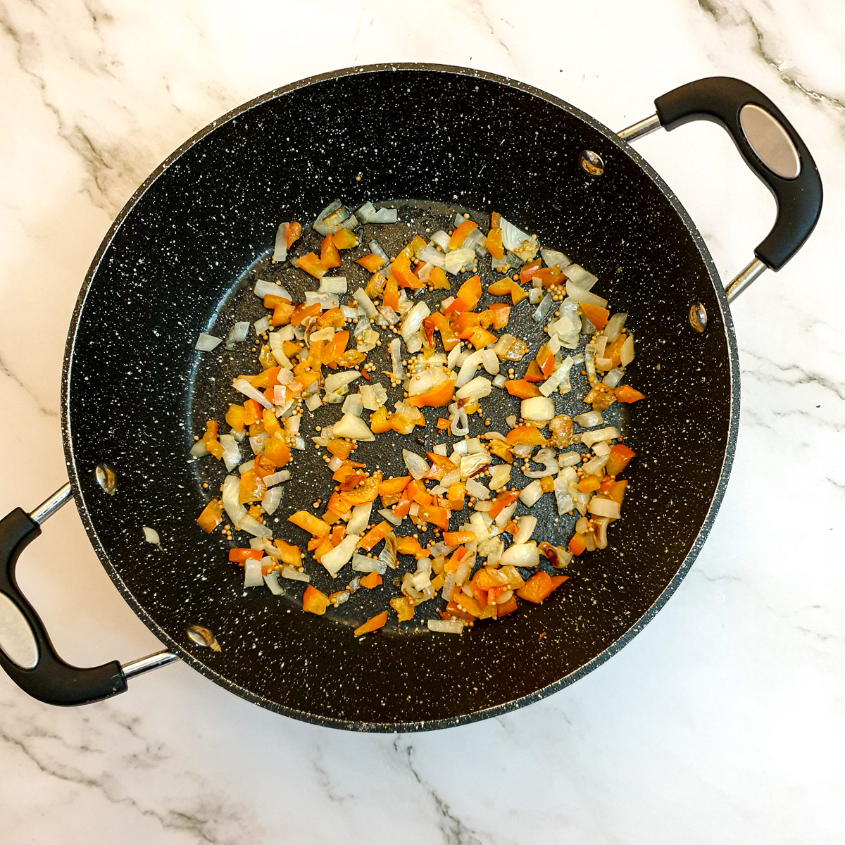 Diced red peppers and onions in a frying pan.