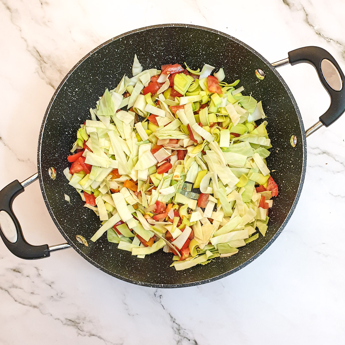 Shredded cabbage and leeks with tomatoes in a frying pan.