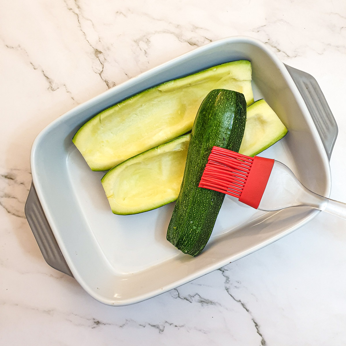 Hollowed out courgettes being brushed with oil.