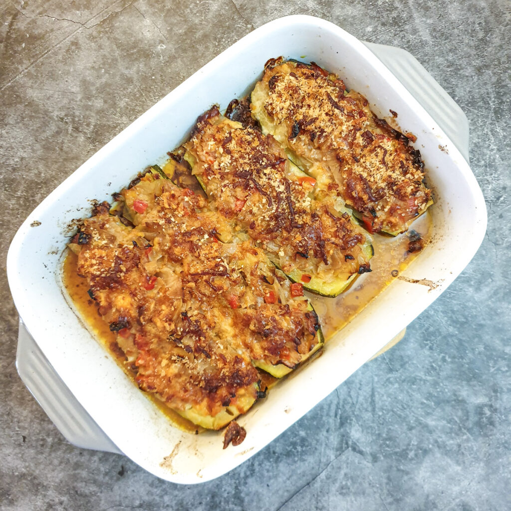 4 baked stuffeed courgettes in a baking dish.