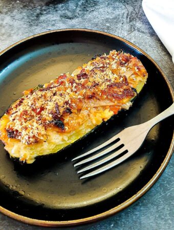 A cabbage-stuffed courgette with a cheesy topping on a brown plate with a fork.