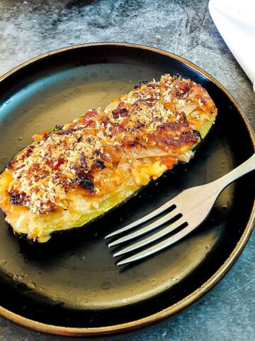 A cabbage-stuffed courgette with a cheesy topping on a brown plate with a fork.