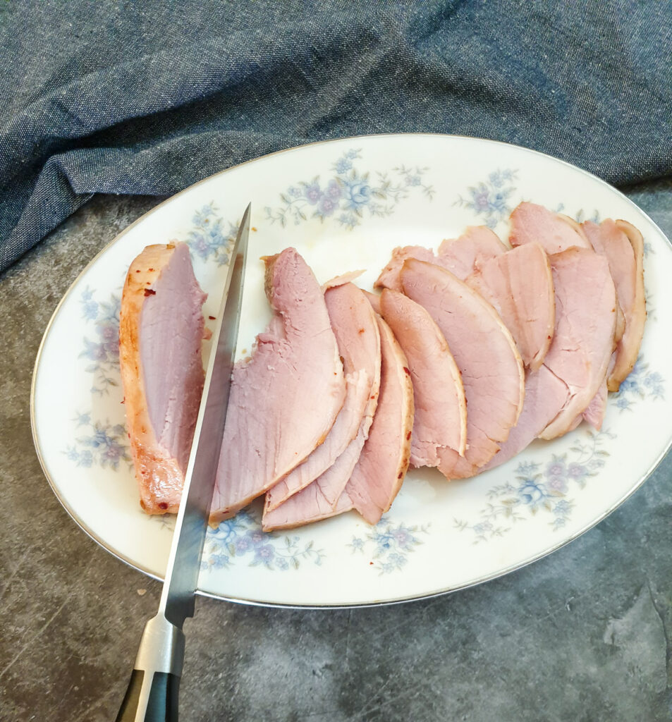 Oven-baked gammon being sliced with a carving knife.