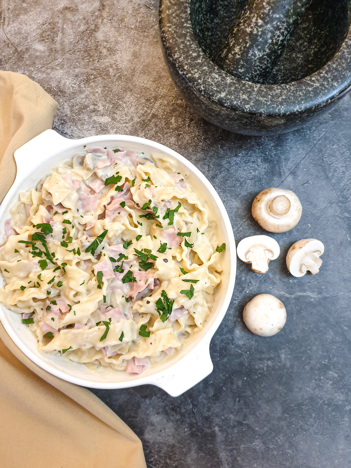 A dish of ham and mushroom tagliatelle next to raw mushrooms.
