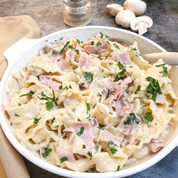 Ham and mushroom tagliatelle in a dish on a table with a few mushrooms in the background.