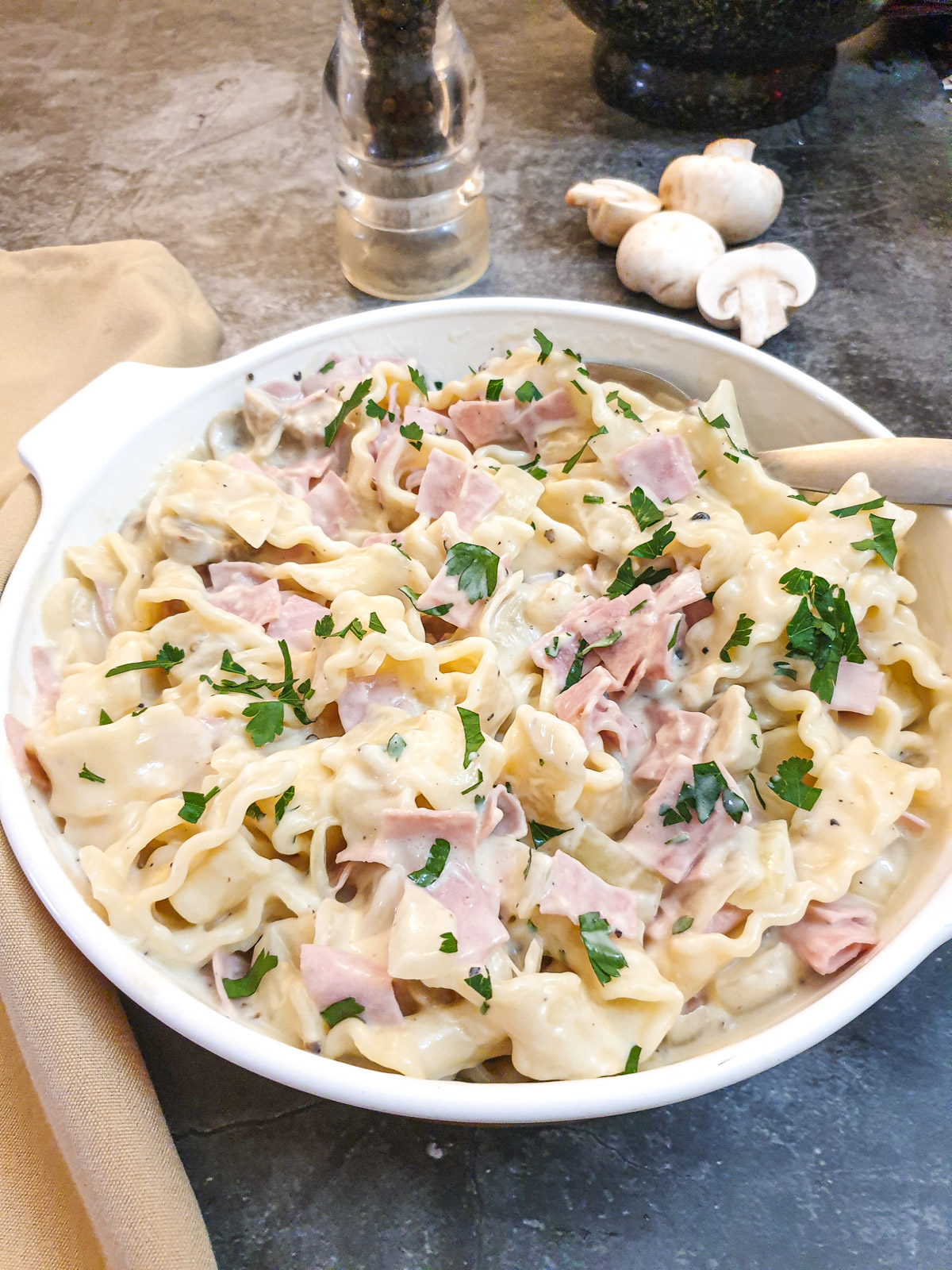 Ham and mushroom tagliatelle in a dish on a table with a few mushrooms in the background.