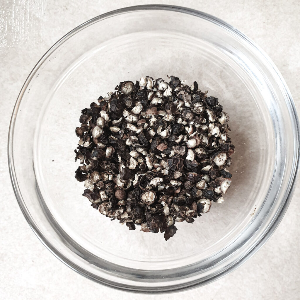 Cracked black peppercorns in  glass dish.