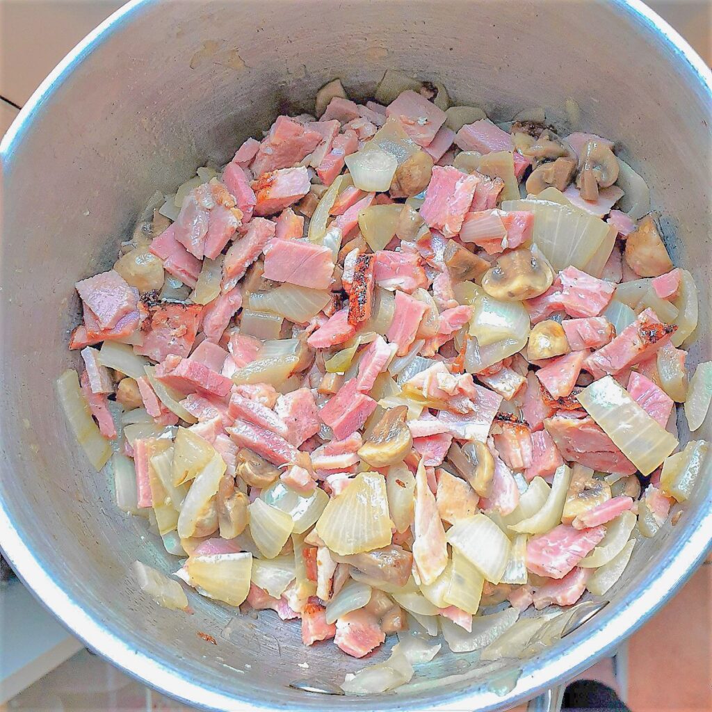 Chopped ham, mushrooms and onions in a saucepan.