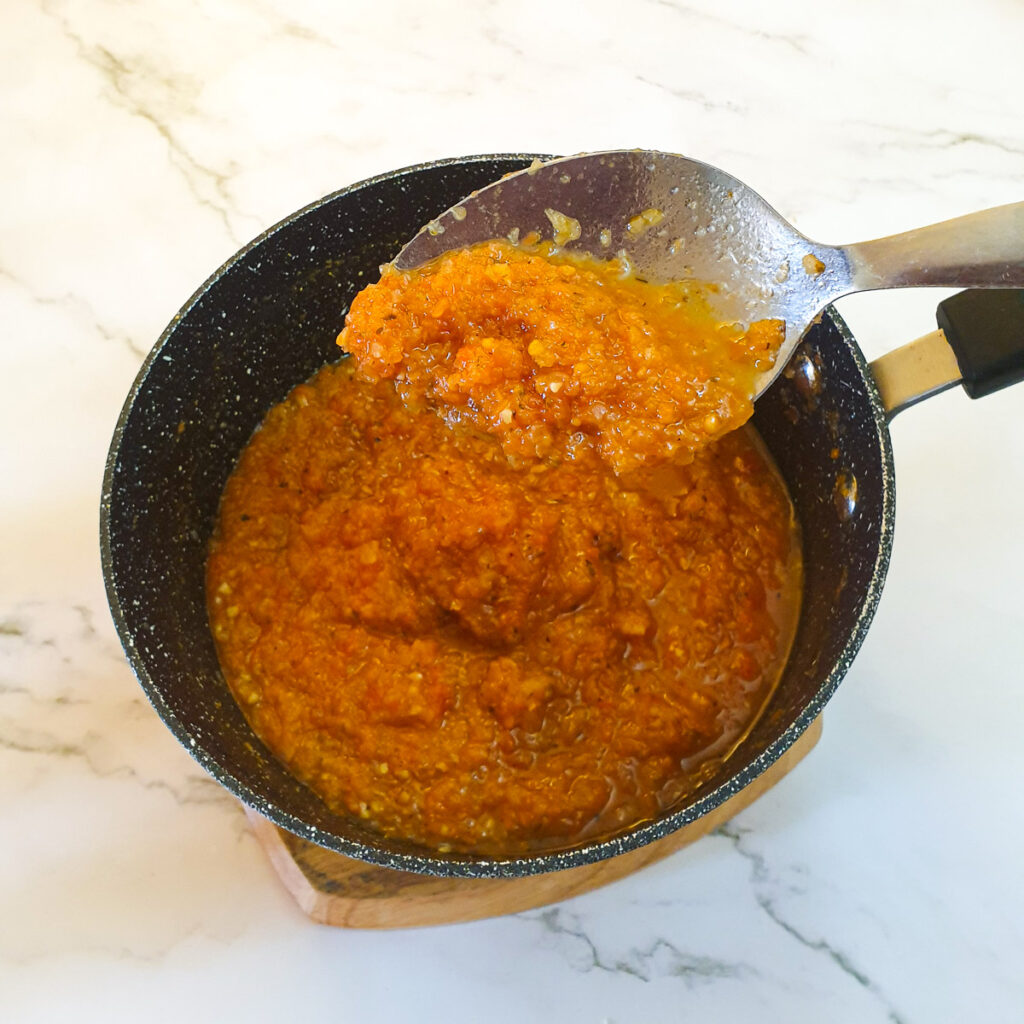 A spoonful of marinara sauce held over a saucepan, showing the consistency.