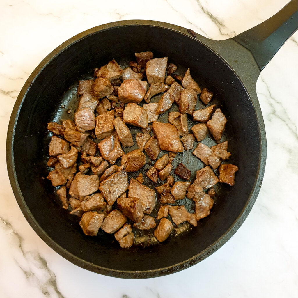 Diced beef being seared in a frying pan.