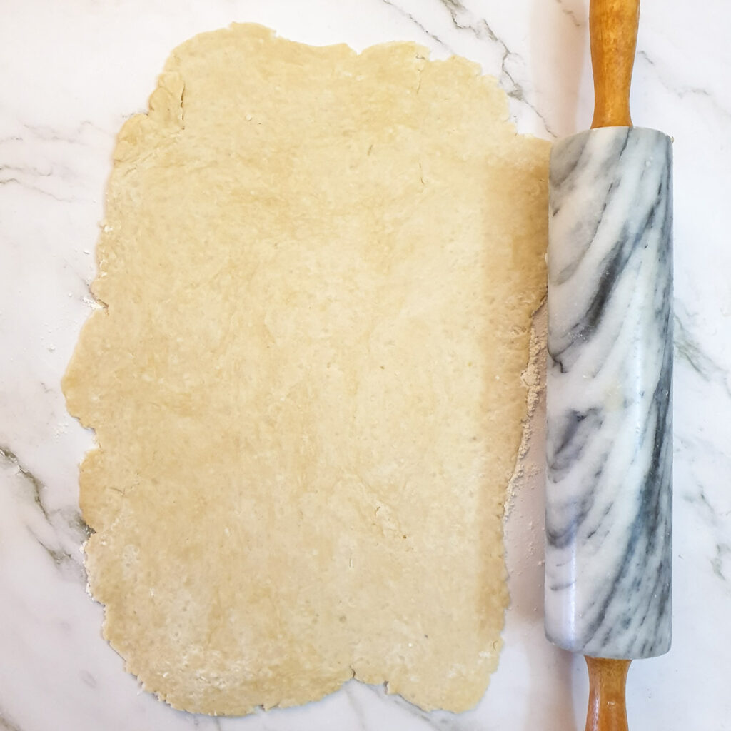 Suet pastry rolled into a rectangle next to a rolling pin.