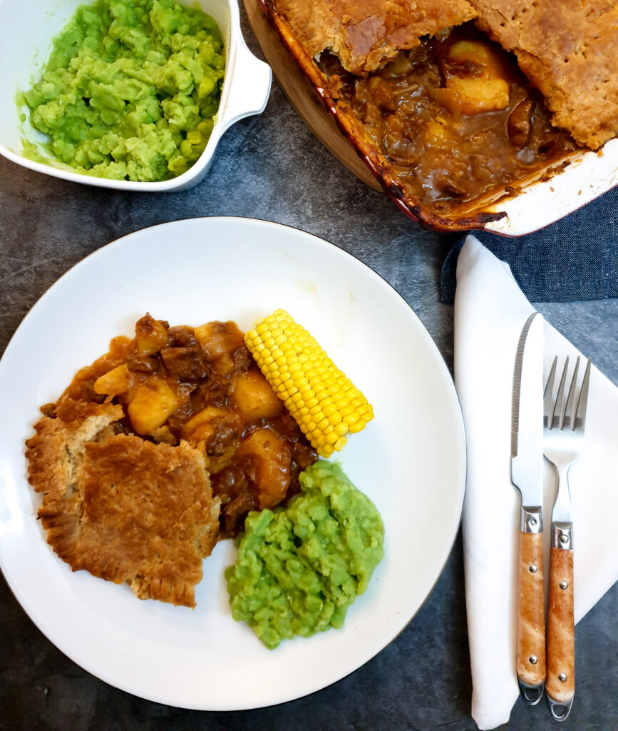 Overhead shot of meat and potato pie on a plate with vegetables.