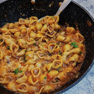 Cheesy mince pasta in a large pan with a spoon.