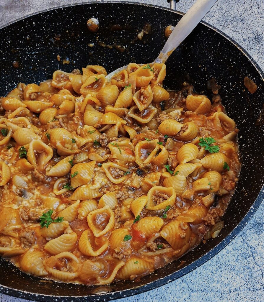 Cheesy mince pasta in a large pan with a spoon.